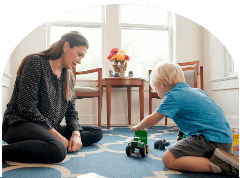 Dr. Maggie Parker sits in floor watching a child play during play therapy